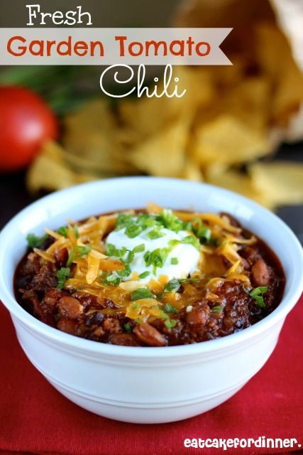 a white bowl filled with chili and cheese on top of a red cloth next to chips