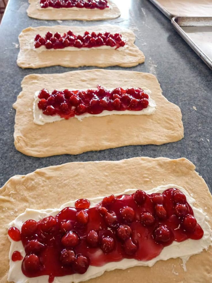 four uncooked pizza doughs with strawberries and cream on them, ready to go into the oven