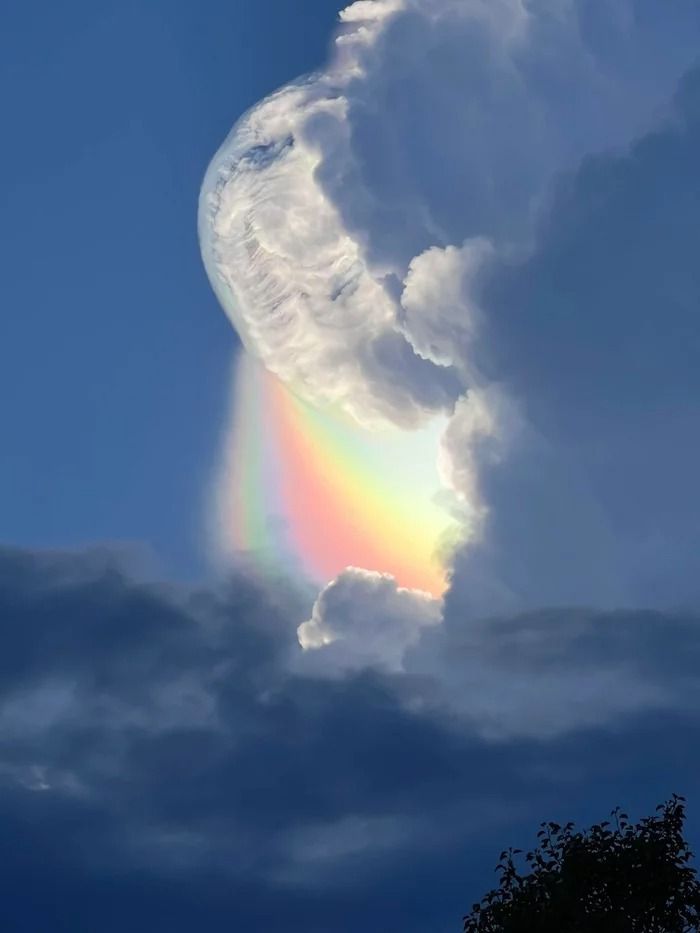 a rainbow appears in the clouds as it is partially obscured by a dark blue sky