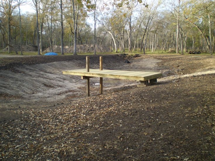 a wooden bench sitting in the middle of a dirt field next to trees and grass