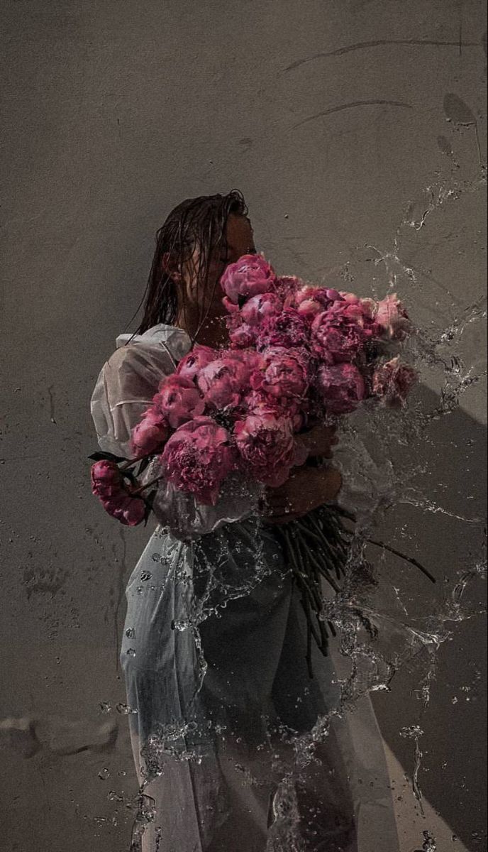 a woman holding flowers in her hands and splashing water all over her face while standing against a wall