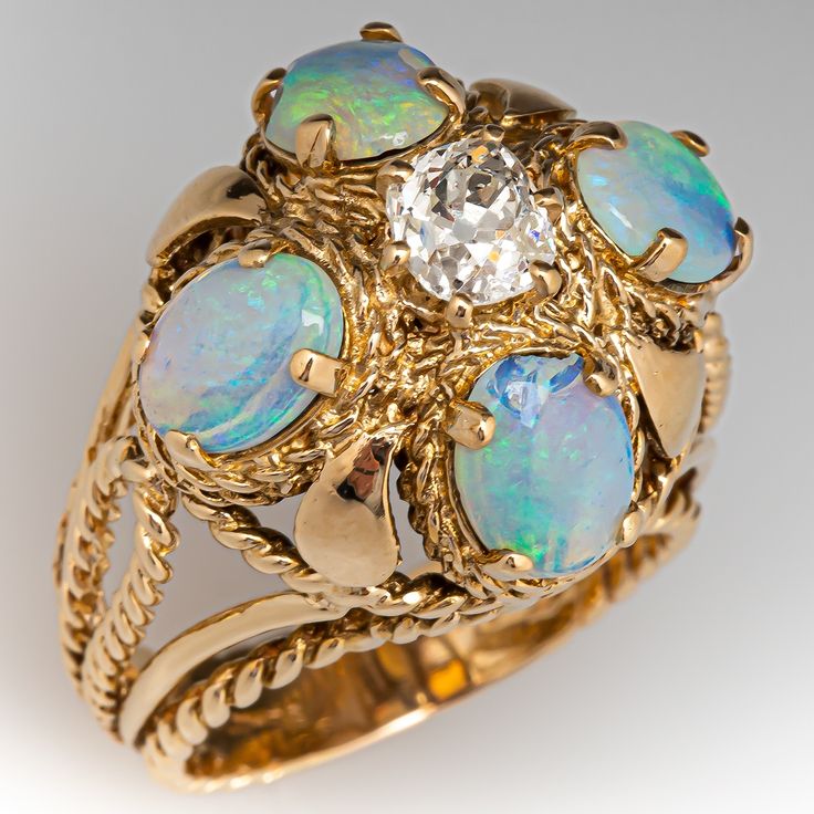 This beautiful vintage ring features an openwork design and is centered with one (1) old mine cut diamond set into a six-prong setting. The center stone is bordered with four (4), prong set, oval cabochon cut natural crystal opals. The ring measures 19.9mm at the top, rises 16.4mm above the finger, tapering to 5.1mm wide and 1.3mm thick at the base of the shank. It is currently a size 8.5. Two of the opals are chipped but it does not distract from the beauty of this piece. Classic Luxury Yellow Gold Opal Ring, Luxury Heirloom Green Opal Ring, Victorian Opal Cluster Ring, Luxury Formal Opal Ring With Oval Cabochon, Luxury Classic Oval Cabochon Opal Ring, Luxury Cabochon Opal Ring, Luxury Women's Cabochon Opal Ring, Antique Oval Cluster Ring With Diamond Accents, Victorian Cluster Ring With Diamond Accents, Oval Shape