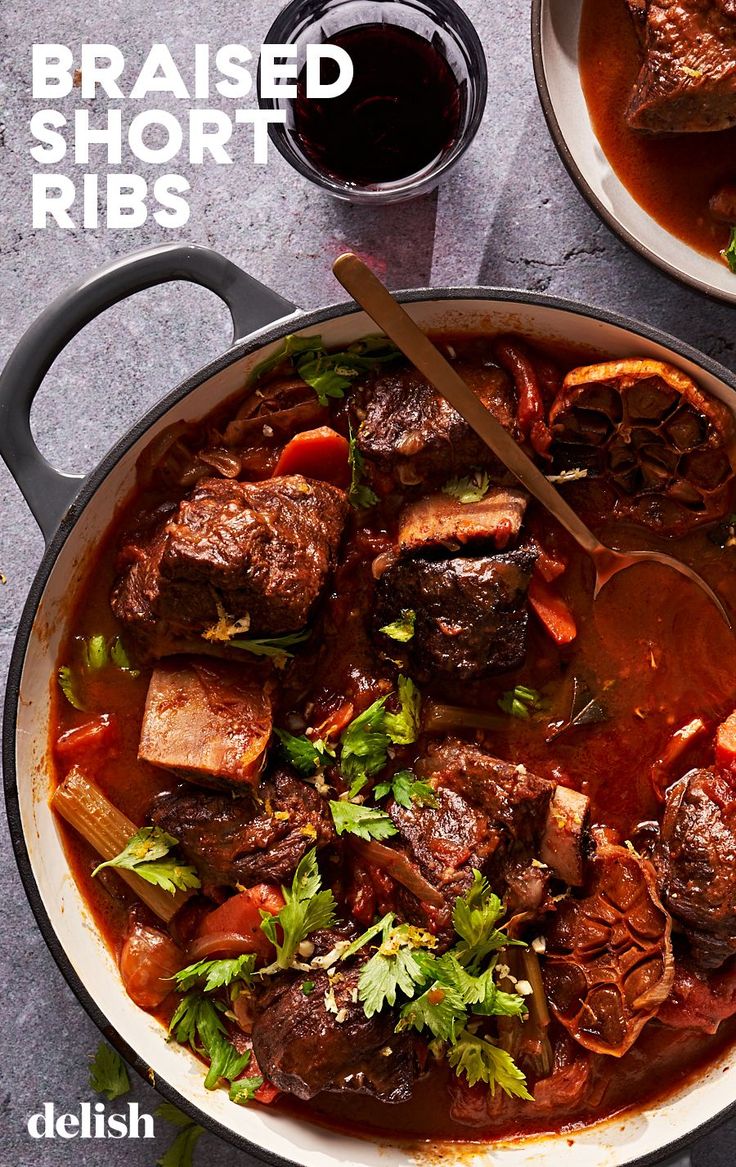 two bowls filled with meat and vegetables on top of a gray table next to a glass of wine