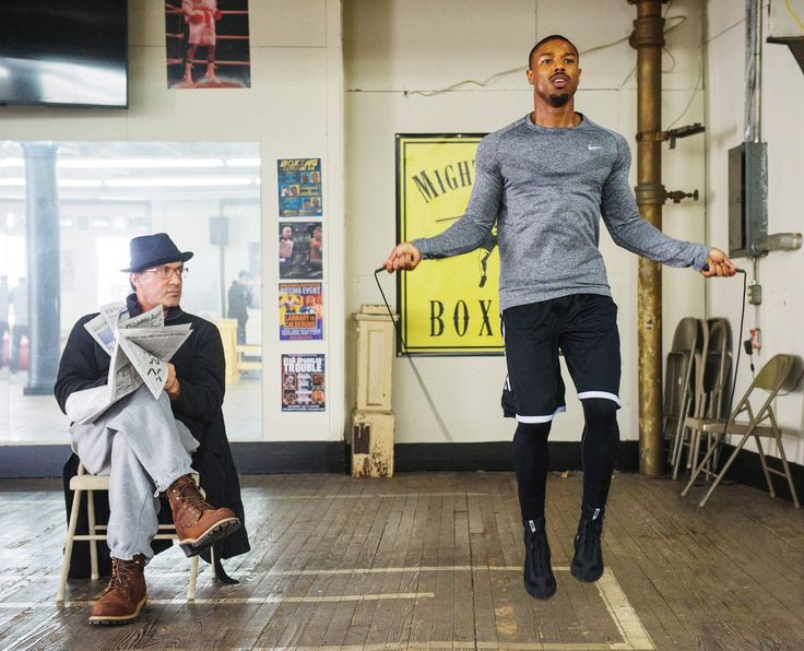 a man is jumping in the air while another man sits on a chair behind him