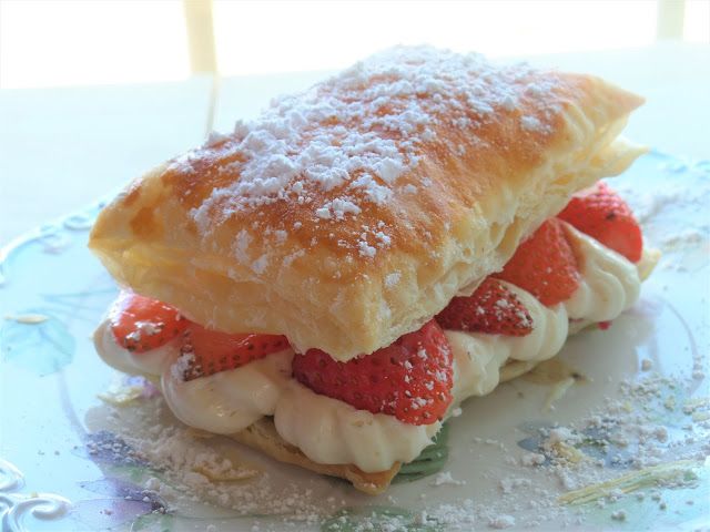 a pastry filled with strawberries on top of a blue and white plate covered in powdered sugar