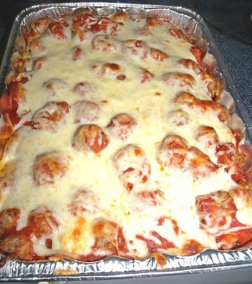 an uncooked pizza covered in cheese and meatballs on top of tin foil