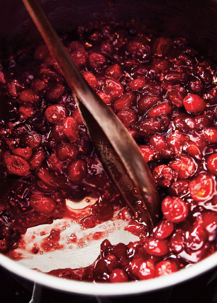 cranberry sauce being stirred in a pot with a wooden spoon