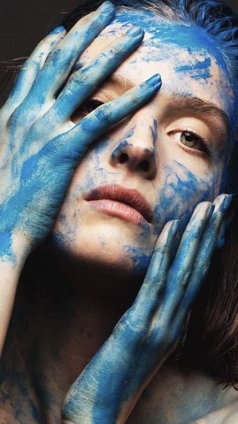 a woman with blue paint on her face holding her hands to her face and covering her eyes