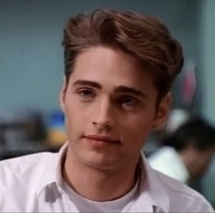 the young man is wearing a white shirt and looking at the camera while sitting down