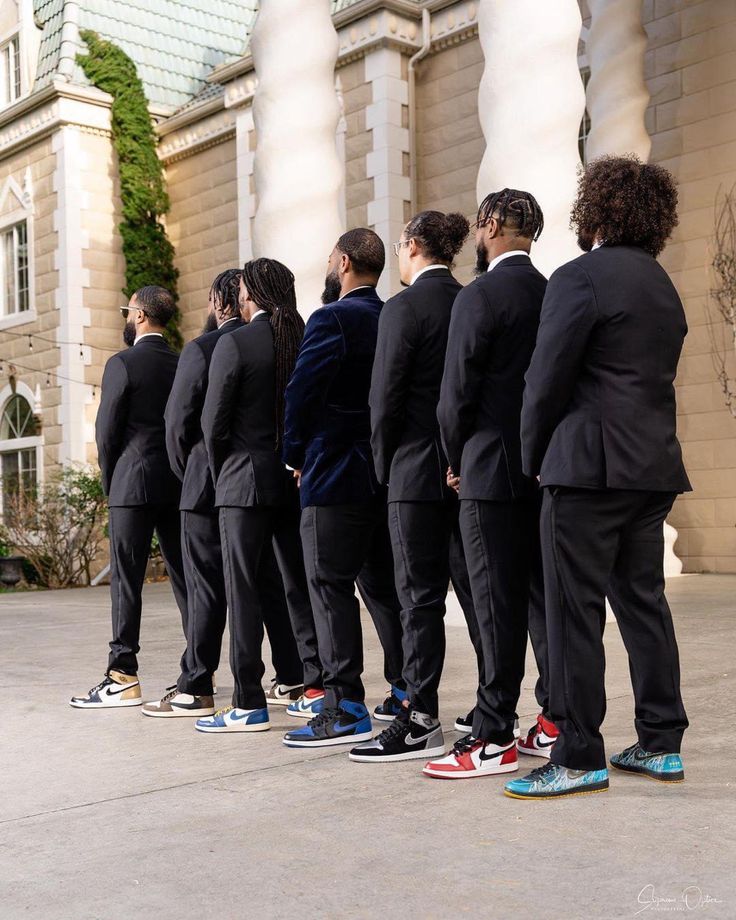 a group of men in suits and sneakers standing next to each other on the sidewalk