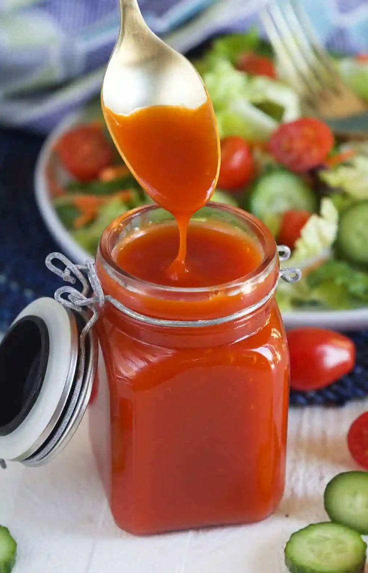 a spoon full of ketchup sitting on top of a table next to a salad