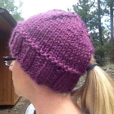 a woman wearing a purple knitted hat in front of a wooden structure and trees