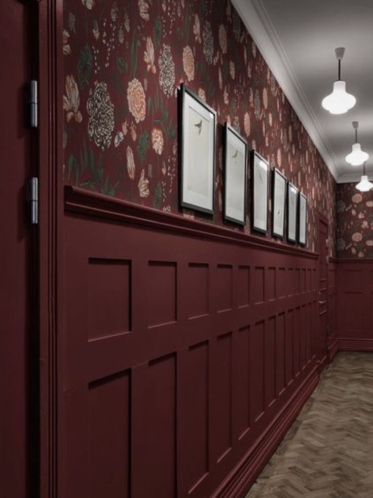 the hallway is lined with red wallpaper and pictures on the walls, along with white lights