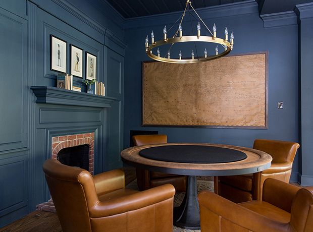 a dining room with blue walls and leather chairs around a round table in front of a fireplace