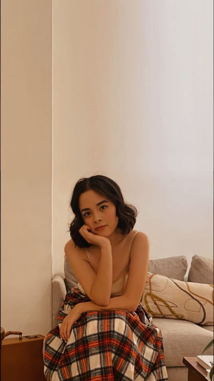 a woman sitting on top of a couch in a living room next to a white wall