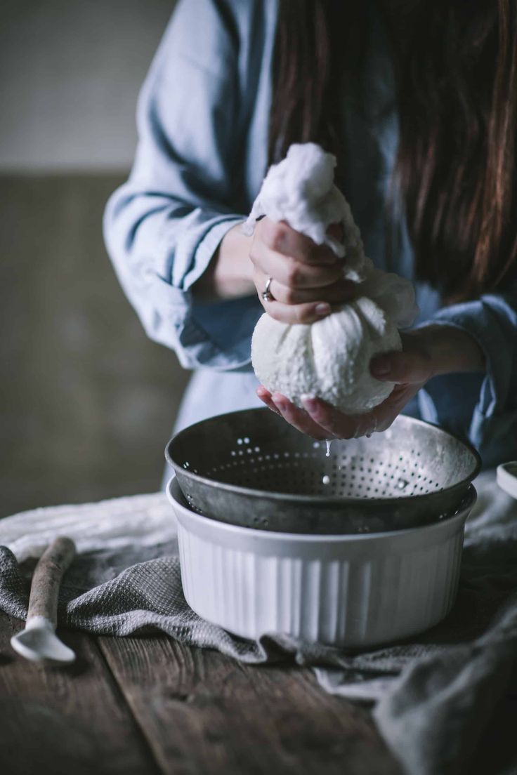 a woman is using a strainer to mix ingredients in a bowl on top of a wooden table