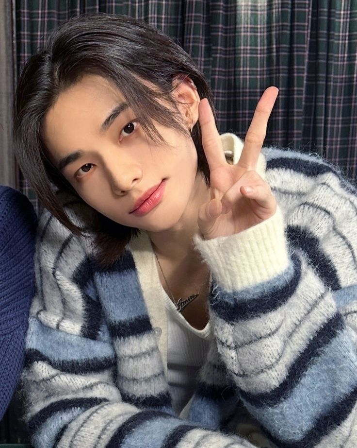 a person sitting on a couch making the peace sign with their hand while wearing a blue and white striped sweater