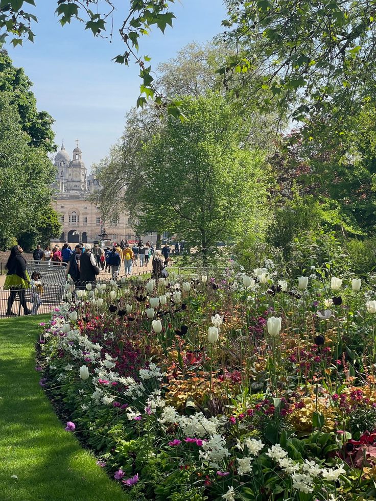 many people are walking through the park with lots of flowers in front of them on a sunny day