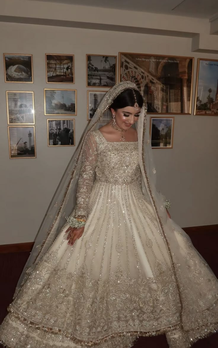 a woman in a white wedding dress standing next to a wall with pictures on it