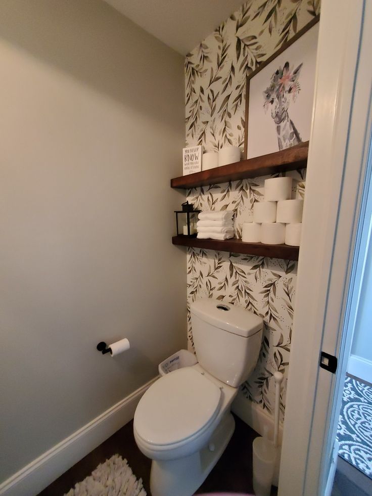 a white toilet sitting inside of a bathroom next to a shelf filled with rolls of toilet paper