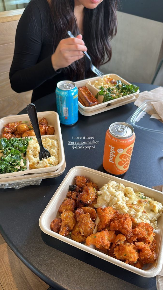 a woman sitting at a table with two trays of food