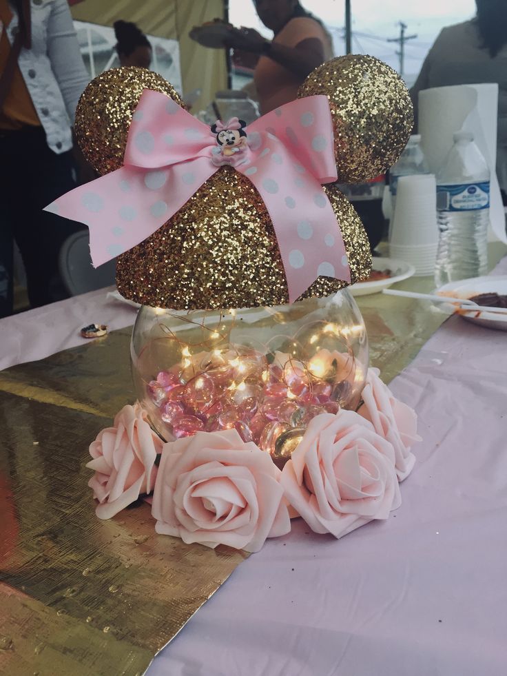 there is a glass vase with pink flowers in it and minnie mouse ears on the table