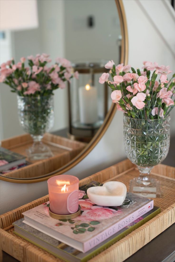 pink flowers are in vases on a table with a mirror and candle next to it