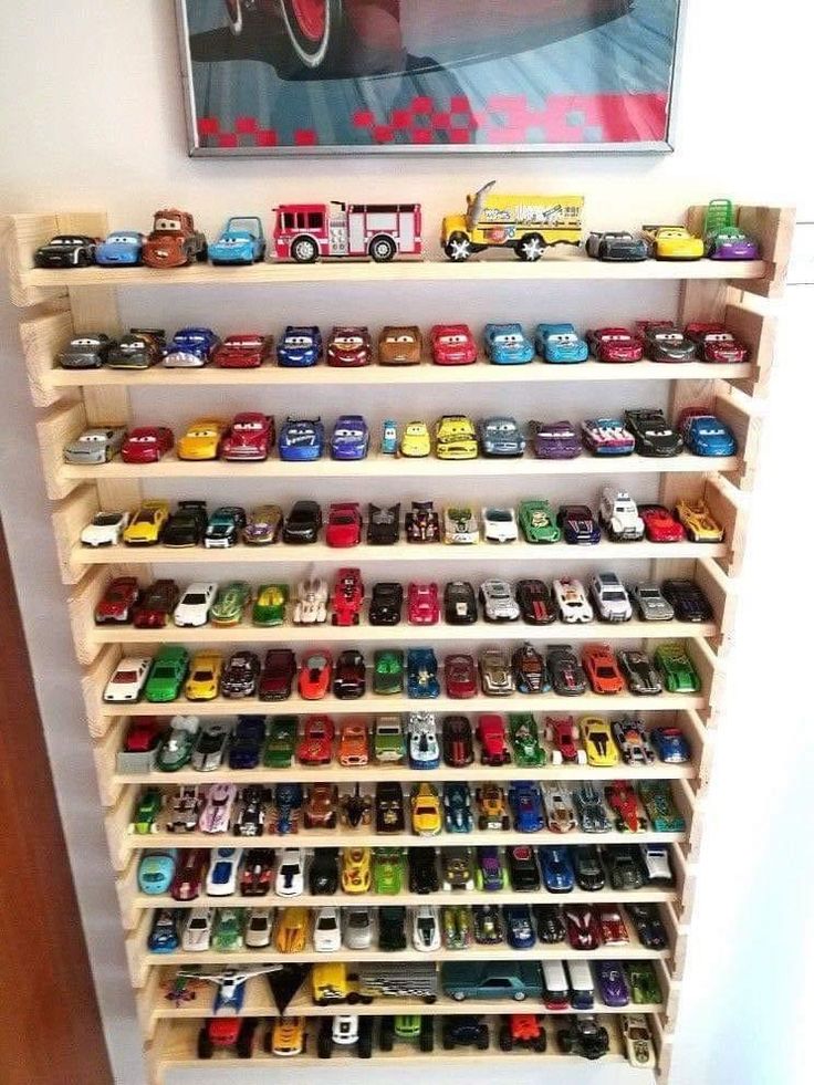 a shelf filled with lots of toy cars next to a painting hanging on the wall