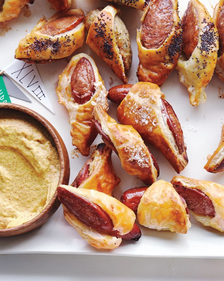 hotdogs and other food items on a tray with dipping sauce in a bowl