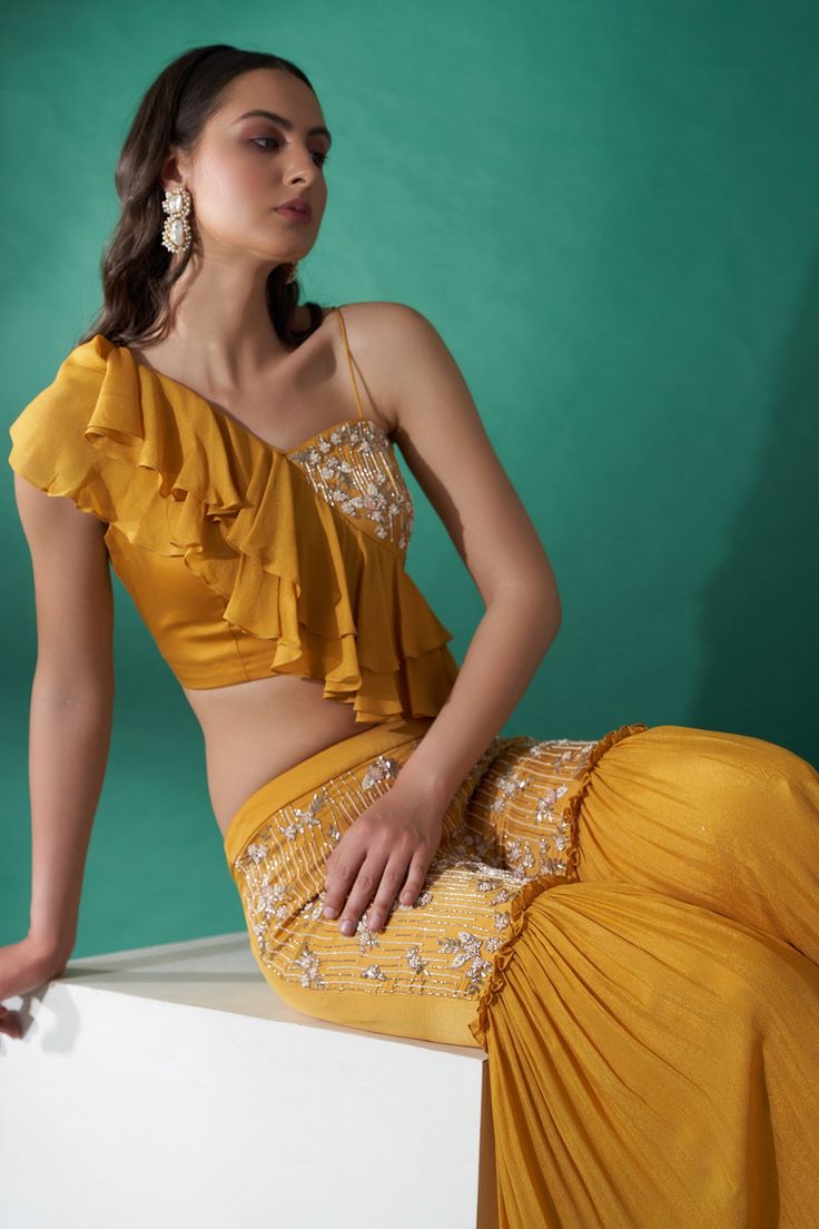 Mustard yellow crop top with ruffle details and hand embroidered floral motifs. Paired with flared pant.
Component: 2
Pattern: Embroidered
Type Of Work: Floral Motifs
Sleeve Type: Sleeveless
Fabric: Satin
Color: Yellow
Other Details: 
Ruffled crop top
Padded top
Occasion: Destination Wedding - Aza Fashions Festive Yellow Pant Set For Party, Festive Yellow Party Pant Set, Traditional Summer Pre-draped Saree With Ruffles, Traditional Pre-draped Saree With Ruffles For Summer, Festive Yellow Ruffled Sharara, Summer Anarkali Sharara With Ruffles, Anarkali Style Sharara With Ruffles For Summer, Traditional Yellow Ruffled Sharara, Summer Saree Sets With Ruffles