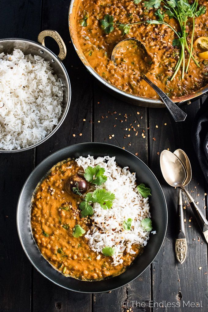 two bowls filled with curry and rice next to silver spoons on a wooden table