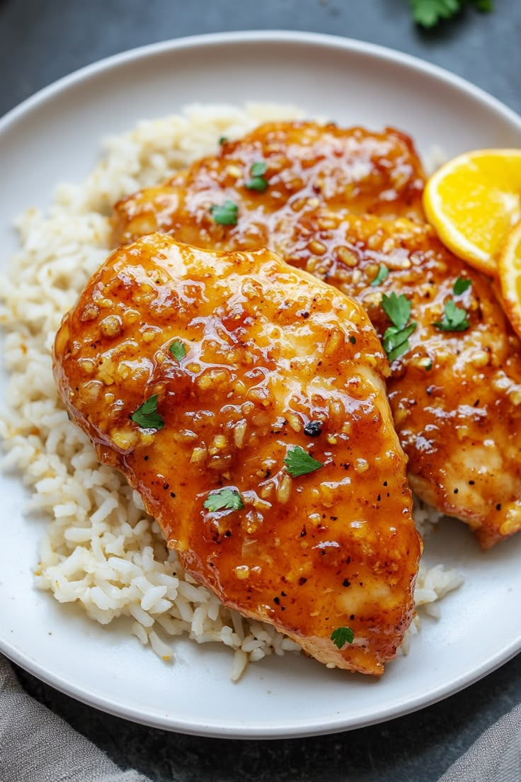 two pieces of chicken and rice on a white plate with garnished lemon wedges