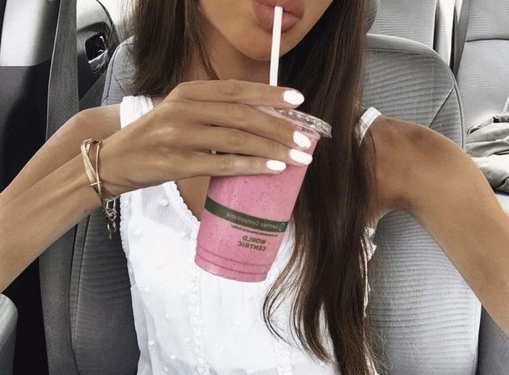 a woman sitting in the back seat of a car drinking from a pink drink cup