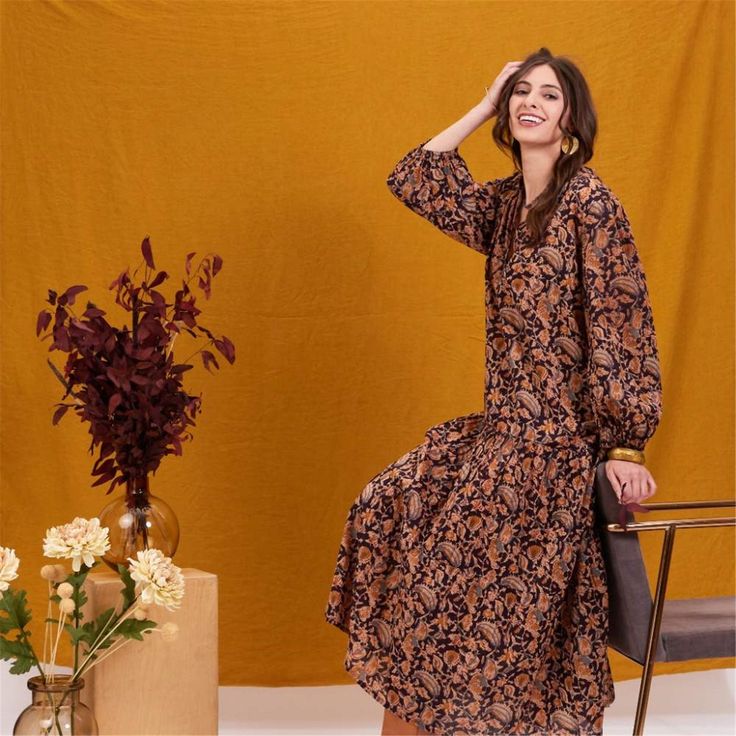 Add a splash of joy to your wardrobe with the Black Spice Madine Drop Waist Maxi Dress! Crafted from 100% cotton, this dress offers a delightfully comfortable fit that drapes beautifully. The vibrant pattern in warm spice tones is both eye-catching and stylish, perfect for making a statement. The full-length sleeves with elastic cuffs add a touch of charm and practicality, while the V-neck mandarin collar gives it an elegant touch. The dress features playful details like long decorative tassels Flowy Cotton Maxi Dress For Fall, Brown Relaxed Fit Dress For Fall, Fall Cotton Dress With Floral Print, Fall Cotton Floral Print Dress, Fall Floral Print Cotton Dress, Brown Relaxed Fit Cotton Dress, Fall Cotton Midi Dress With Floral Print, Orange Bohemian Cotton Midi Dress, Fall Cotton Midi Dress In Brown