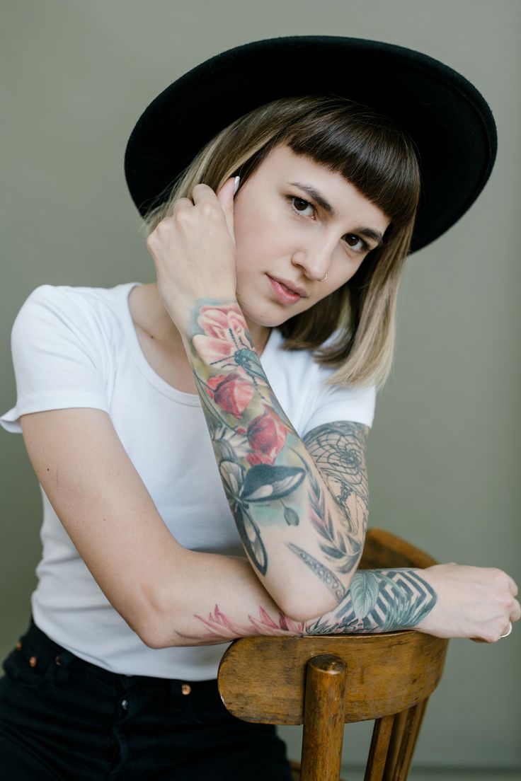 a woman sitting in a chair with tattoos on her arm and arms behind her head