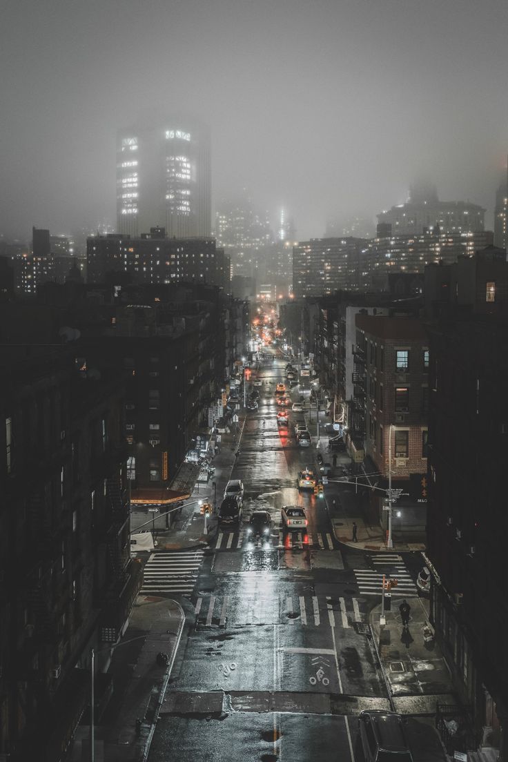 an empty city street at night in the rain with buildings on both sides and lots of traffic