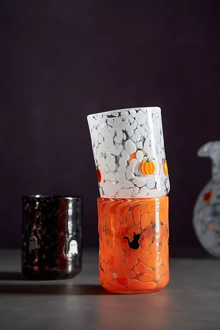 an orange and white vase sitting on top of a table next to a black cup