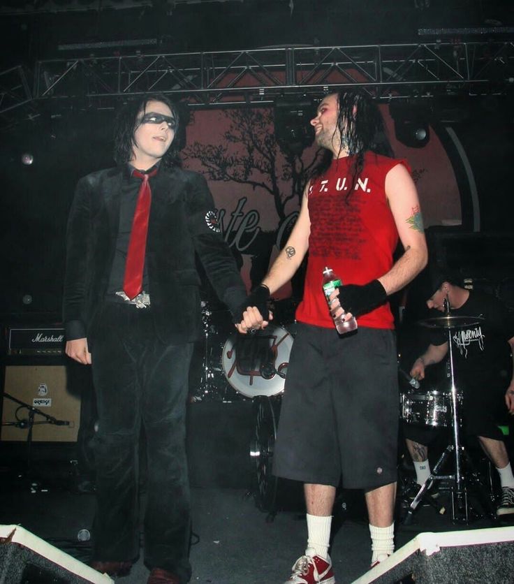 two men dressed in black and red are standing on stage with one holding the other's hand