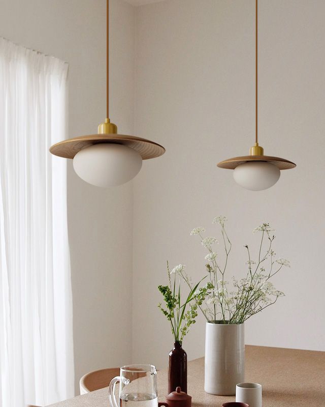 two pendant lights hanging over a table with vases and cups on top of it