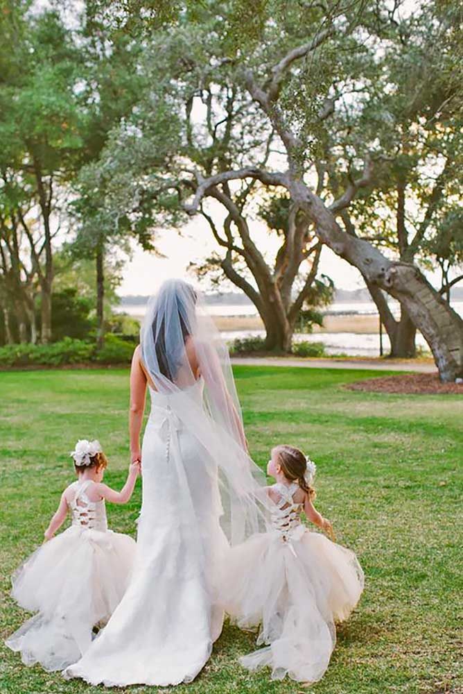 the bride and her two flower girls are walking through the grass with their veil blowing in the wind