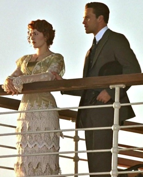 a man and woman standing on the deck of a ship looking at something off to the side