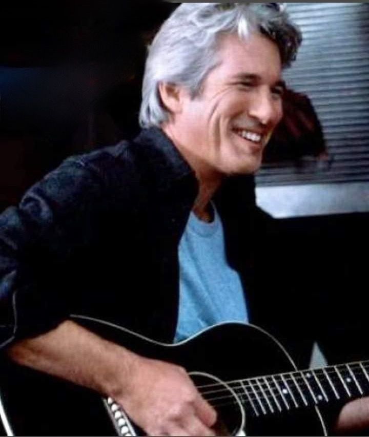 an older man smiles as he plays the guitar