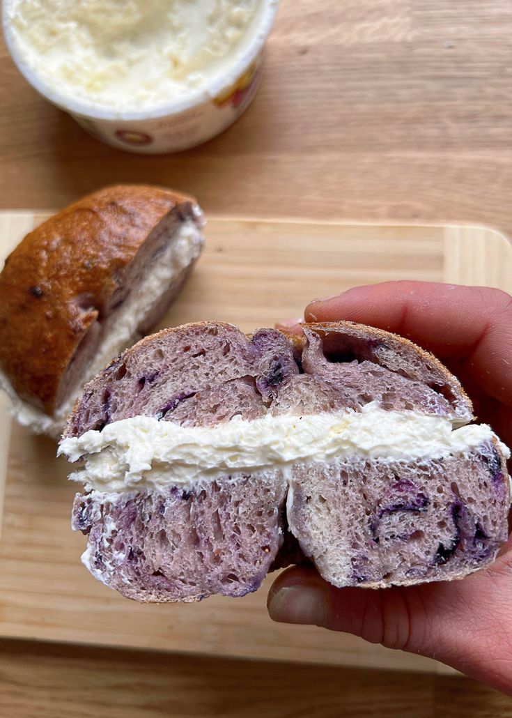 a person holding a half eaten sandwich on a cutting board next to a bowl of yogurt