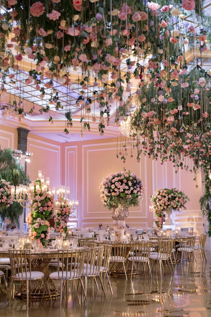 an elegant wedding reception with pink flowers and greenery hanging from the ceiling