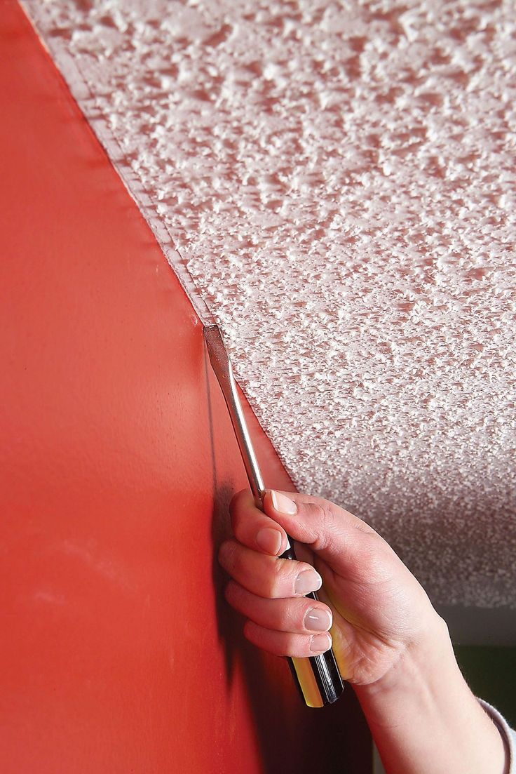 a person holding a pair of scissors near a red wall with water droplets on it