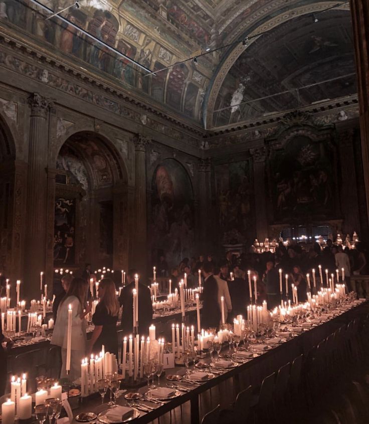 a long table with many lit candles on it in a large room filled with people