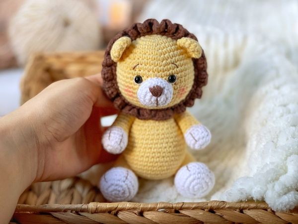 a small crocheted lion sitting in a basket next to a person's hand