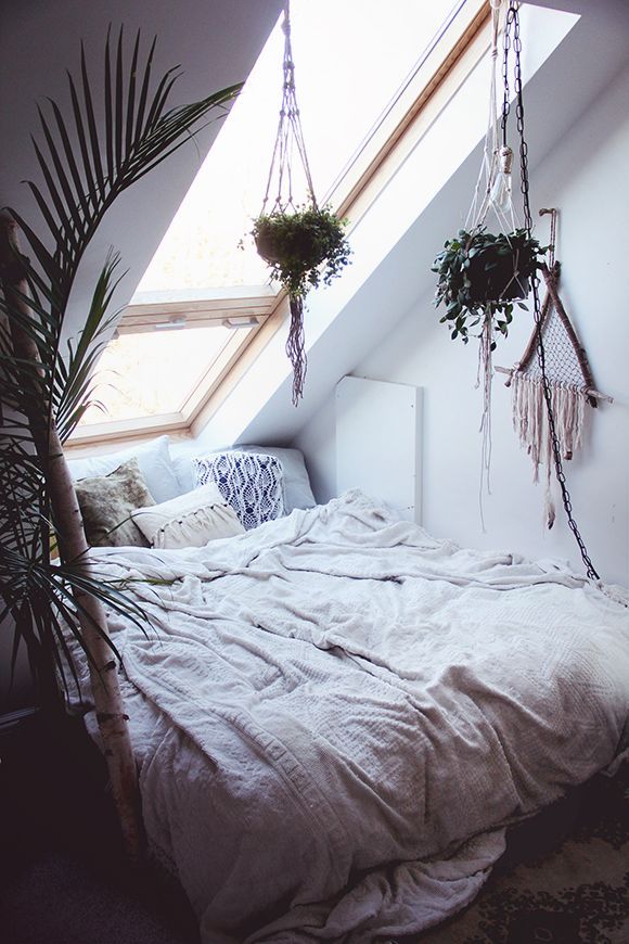 there is a bed with two plants hanging from the ceiling and one has a window above it