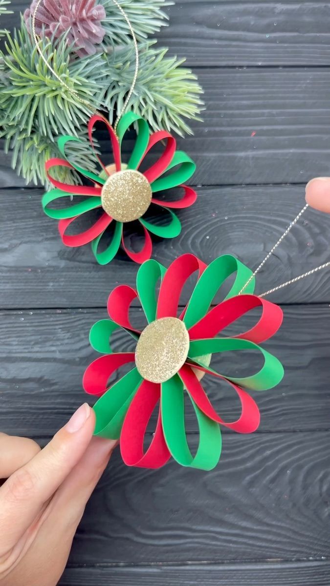 two paper flowers are being held by someone's hand on a wooden table with pine branches