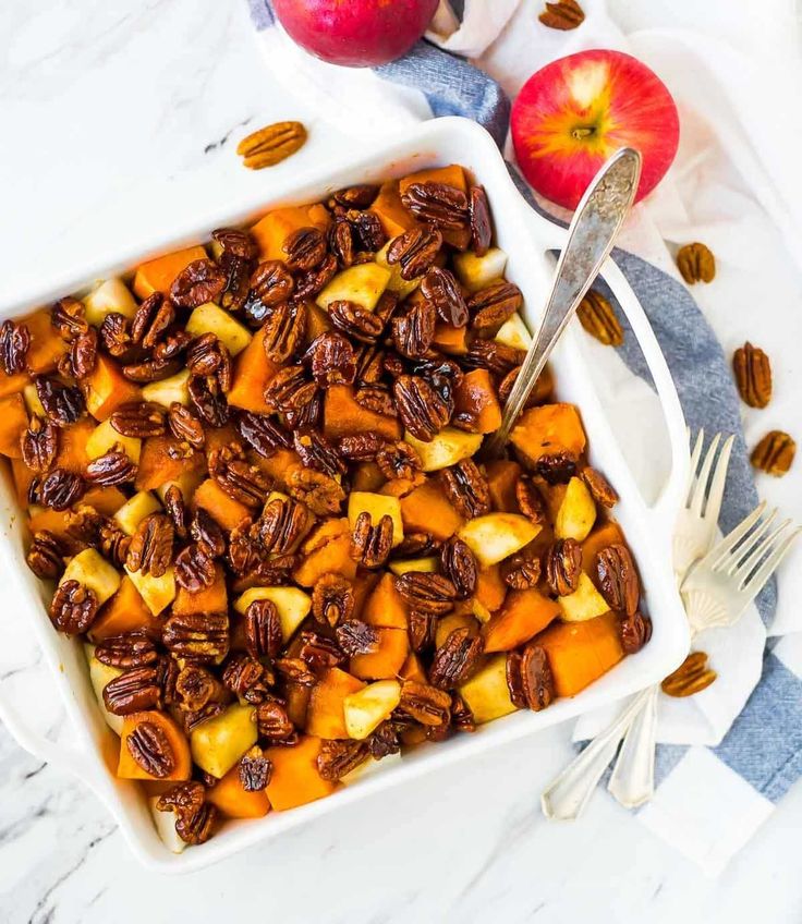 a white casserole dish filled with sweet potatoes and pecans